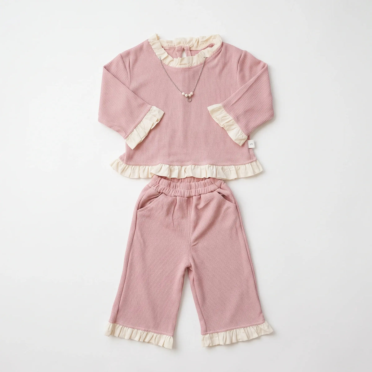 A two-piece baby outfit set in dusty pink corduroy, featuring a long-sleeve top with cream ruffle trim and matching wide-leg pants with ruffle cuffs, laid flat on a white background.