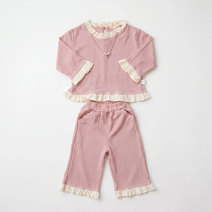 A two-piece baby outfit set in dusty pink corduroy, featuring a long-sleeve top with cream ruffle trim and matching wide-leg pants with ruffle cuffs, laid flat on a white background.