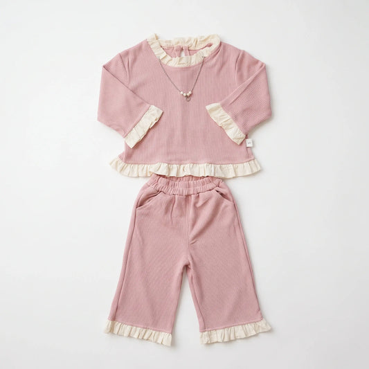 A two-piece baby outfit set in dusty pink corduroy, featuring a long-sleeve top with cream ruffle trim and matching wide-leg pants with ruffle cuffs, laid flat on a white background.