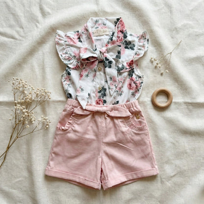 Floral top and pink shorts on a light background with a wooden ring and dried flowers.
