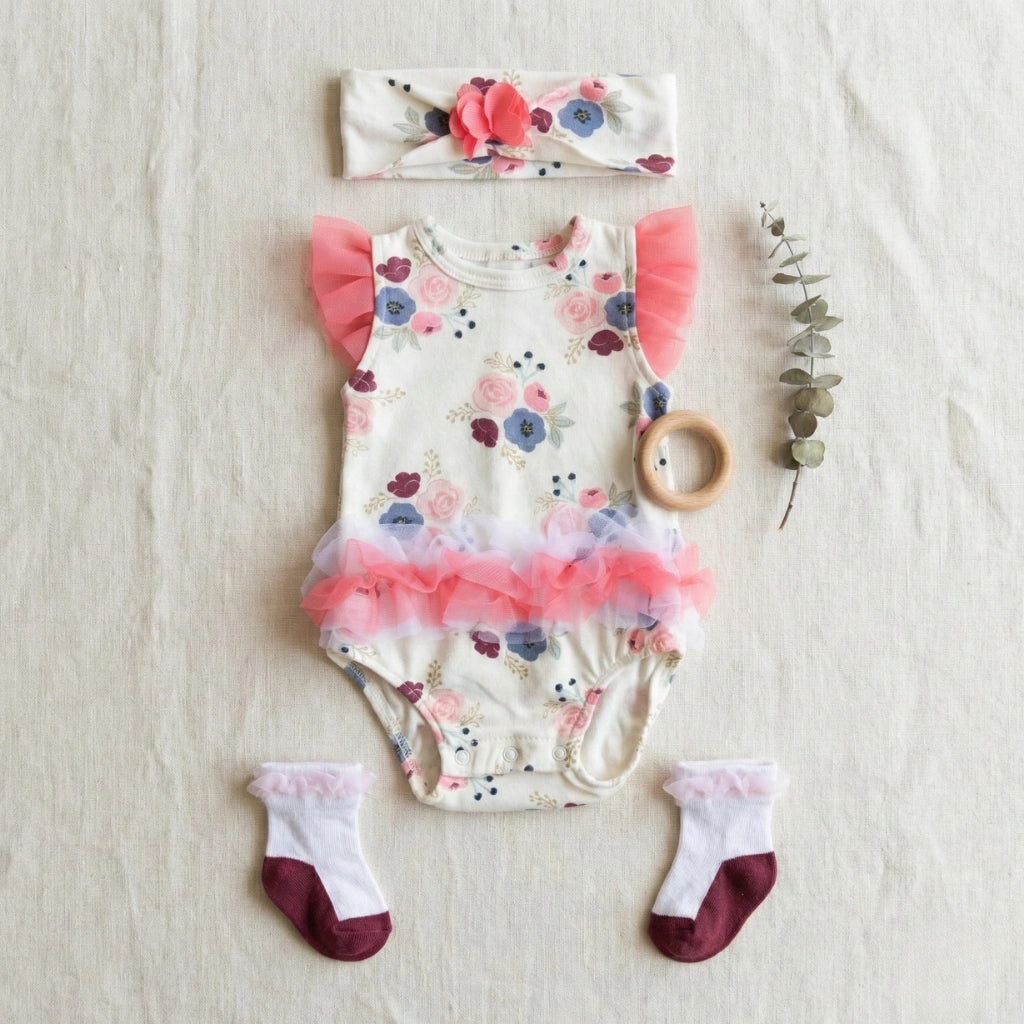 Baby outfit set with floral romper, headband, socks, and wooden teether on a light background