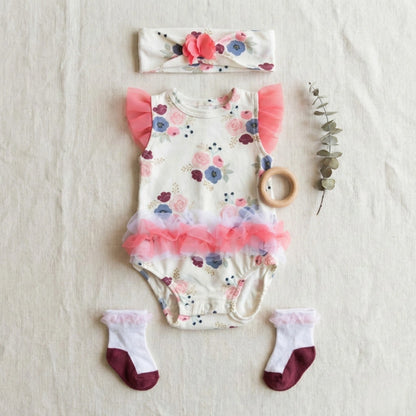 Baby outfit set with floral romper, headband, socks, and wooden teether on a light background