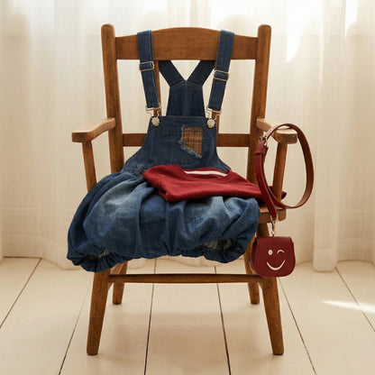 Denim overalls with a red shirt and matching bag on a wooden chair.