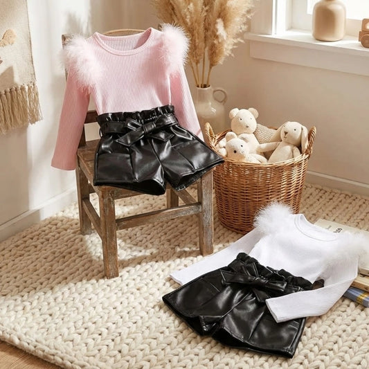 Pink sweater with black leather shorts on a chair, with toys in a basket in the background.