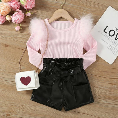 Pink --Pink crop top with fluffy sleeves and black shorts on a wooden surface with flowers and a card.