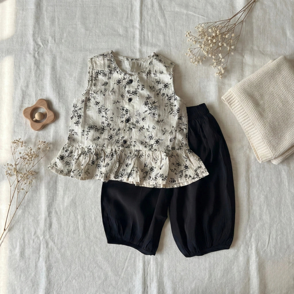 Children's floral top and black pants on a textured surface with dried flowers and a blanket.