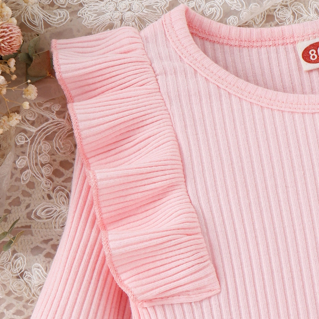 Close-up of a pink ribbed sweater with ruffled sleeves on a decorative background.