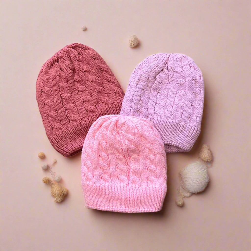 Three knitted hats in pink and purple on a white background
