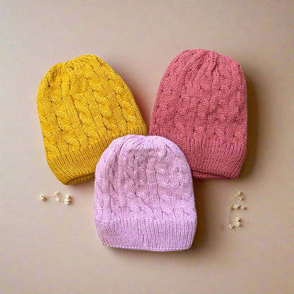 Three knitted hats in yellow, pink, and purple on a white background