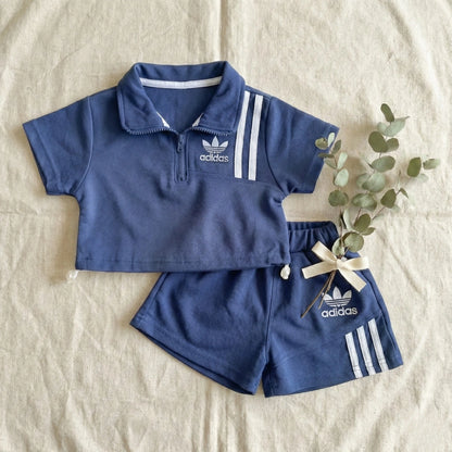 Blue Adidas children's outfit with shorts on a beige surface.