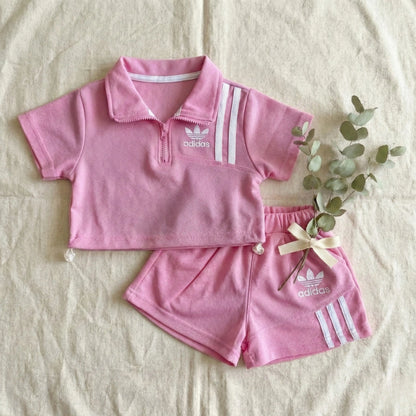 Pink Adidas children's outfit with shorts on a beige surface