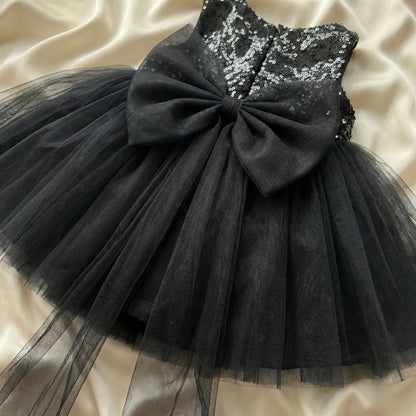 Black dress with sequin top and large bow on a beige fabric background