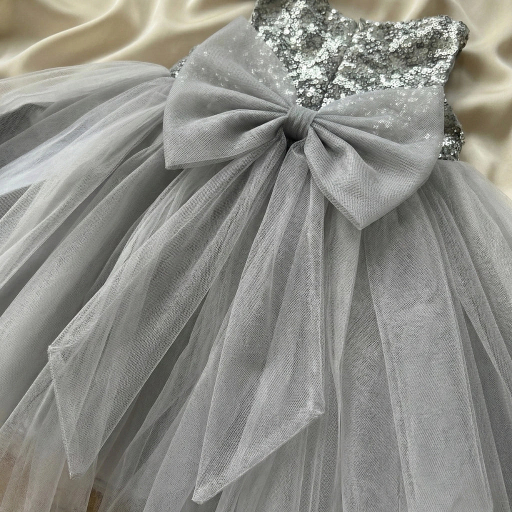 Gray tulle dress with a large bow and sequin top on a beige fabric background