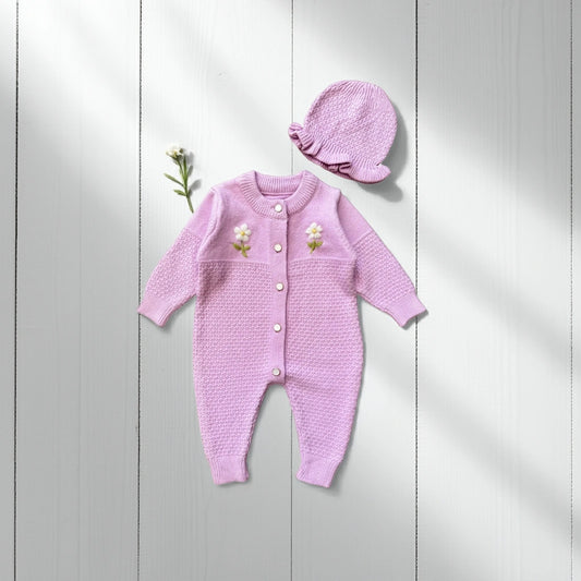 Pink knitted baby outfit with floral details on a light wooden background
