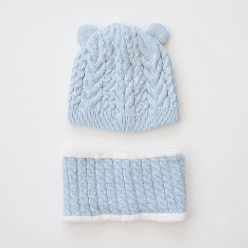 A light blue cable-knit baby beanie with small ear tabs and a matching knit neck warmer, laid flat on a white background.