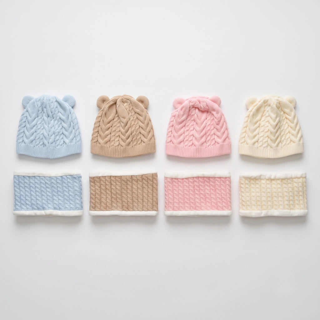 Four cable-knit baby hats with ear details in light blue, tan, pink, and cream, displayed above matching knit neck warmers on a light gray background.