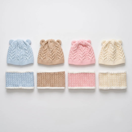 Four cable-knit baby hats with ear details in light blue, tan, pink, and cream, displayed above matching knit neck warmers on a light gray background.