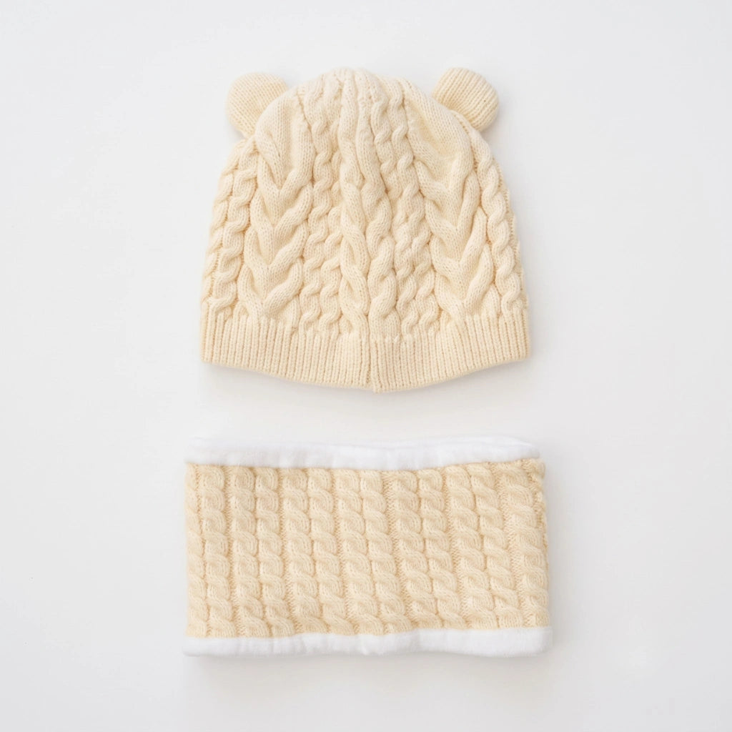 A cream-colored cable-knit baby hat with two bear ears and a matching knit neck warmer with white faux fur trim, displayed on a clean white background.