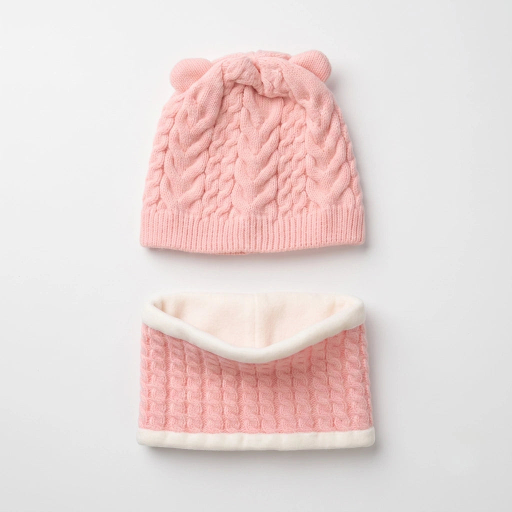 A baby knit hat and matching neck warmer set in soft pink and cream. The hat features a cable-knit pattern, ribbed brim, and two small knotted bear ears on top.