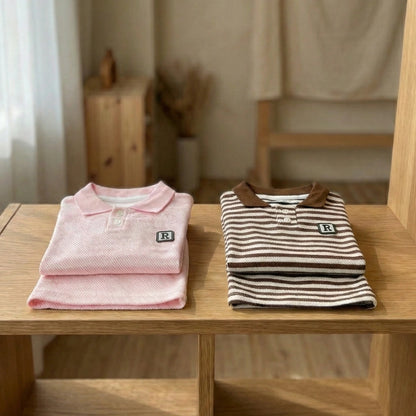 Two folded polo shirts, one pink and one striped, on a wooden surface with a neutral background.