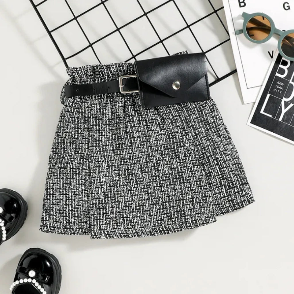 Black and white patterned skirt with a black belt and clutch on a grid background