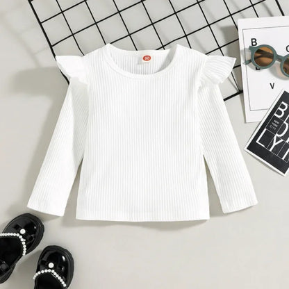 White ribbed long-sleeve top on a light gray surface with sunglasses and a magazine in the background.