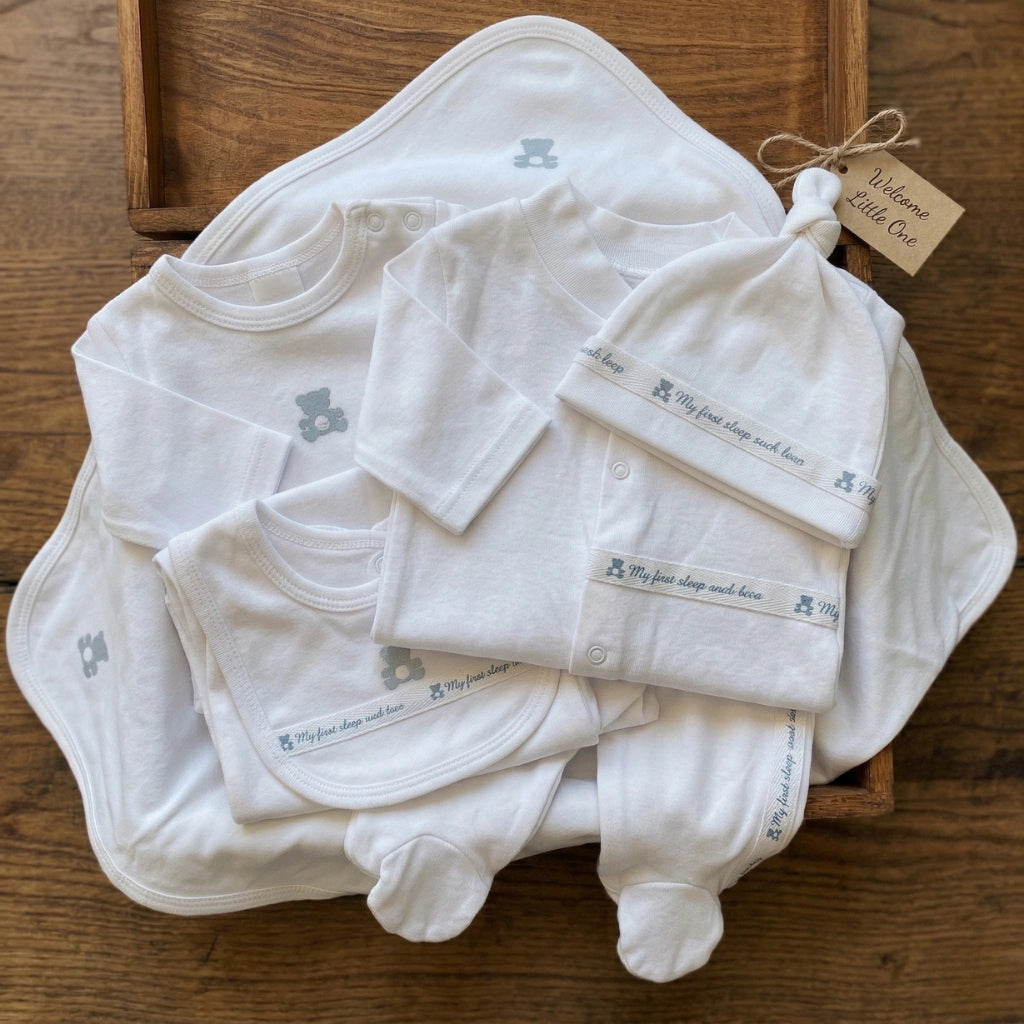 Collection of baby clothes including a hat, onesie, and pants on a wooden surface.