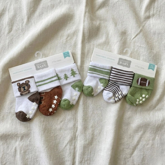 Two sets of baby socks in packaging on a beige fabric background