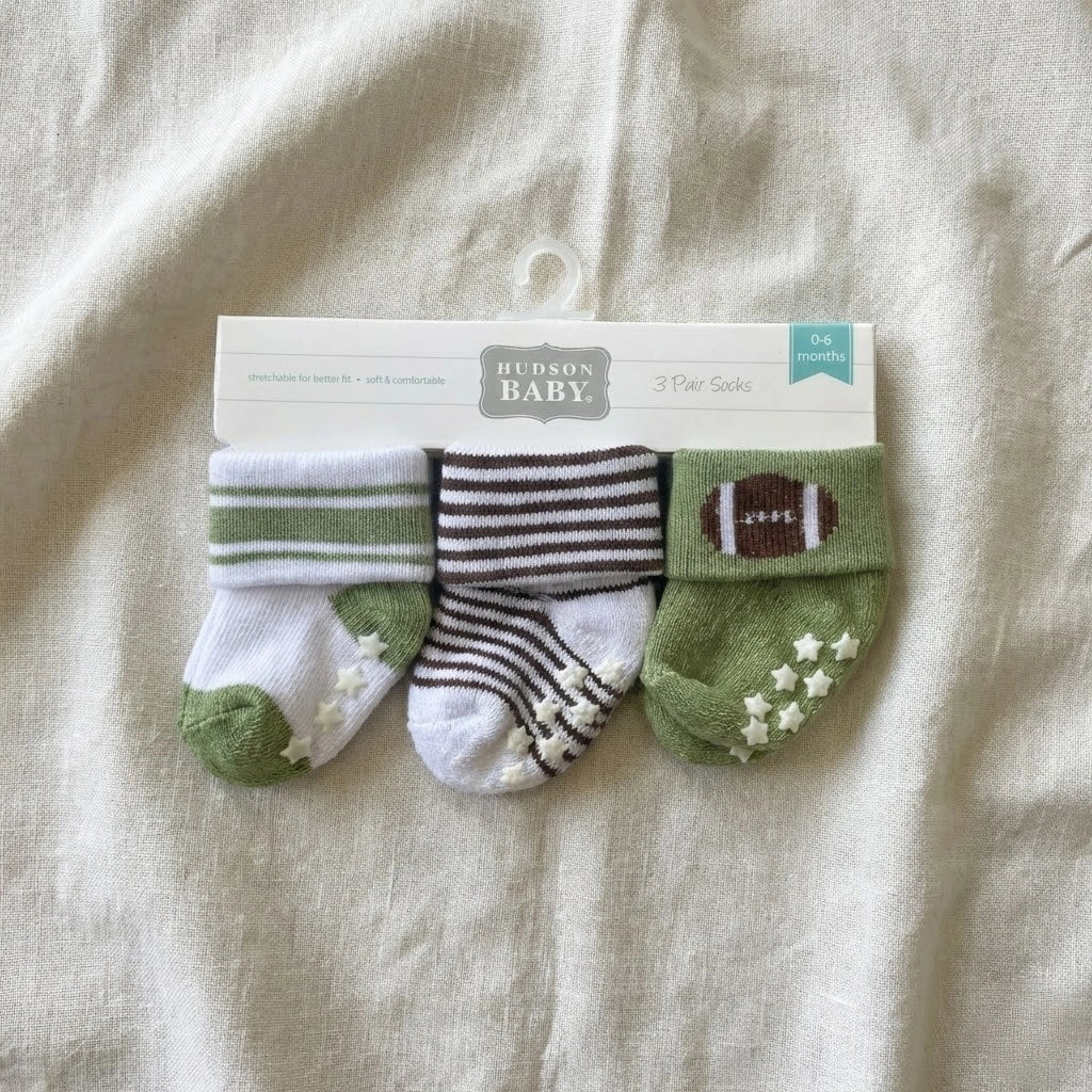Three pairs of baby socks in packaging on a beige fabric background