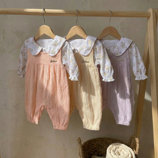 Three baby rompers with lace collars hanging on a rack against a neutral wall.