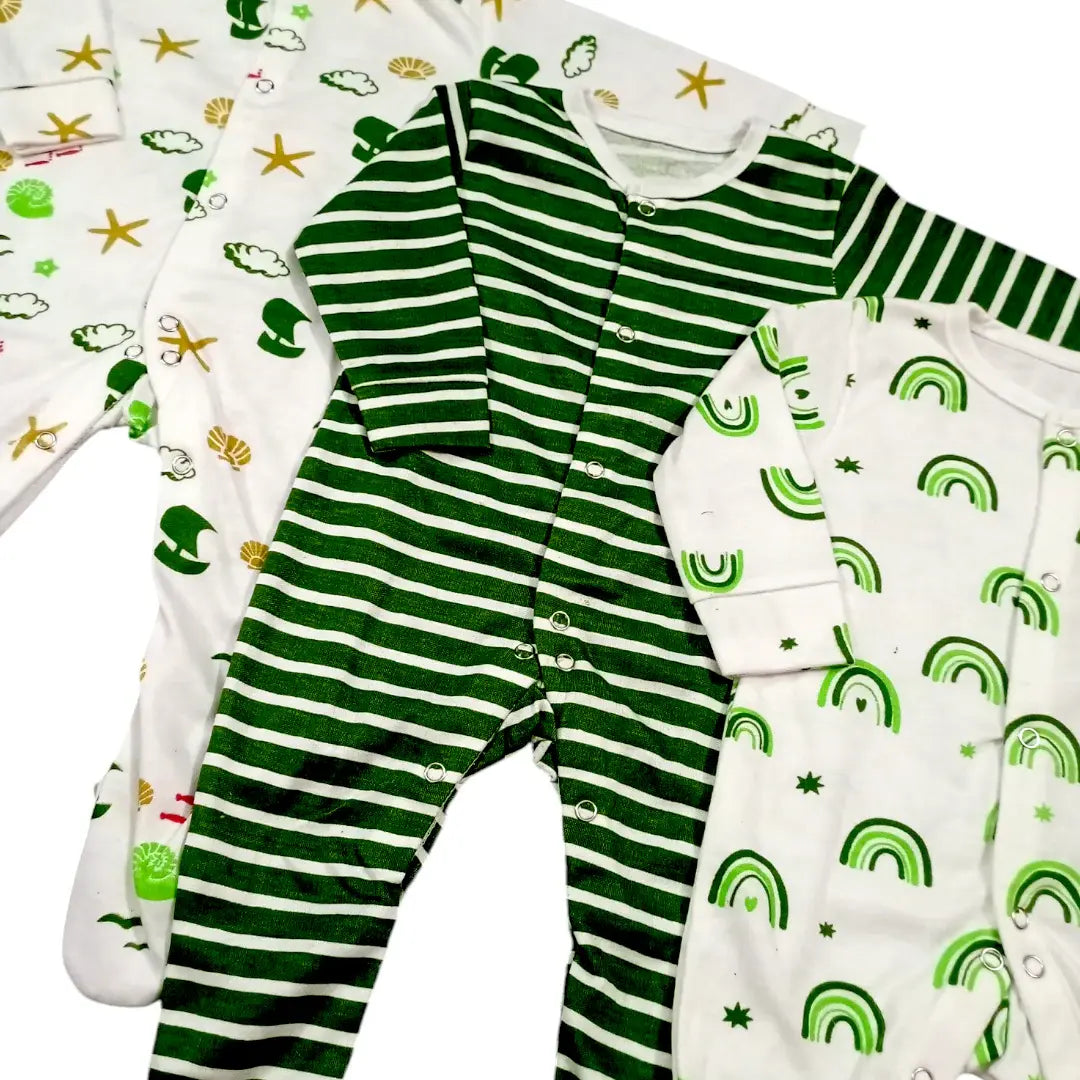 Displayed are the *Alaya Junior Pack Of 3 Winter Baby Rompers – Green Lining*, showcasing two rompers primarily white with rainbow patterns, stars, and playful designs, alongside one romper in green with white stripes. These baby onesies feature snap button closures and are made from soft fabric for ultimate comfort.