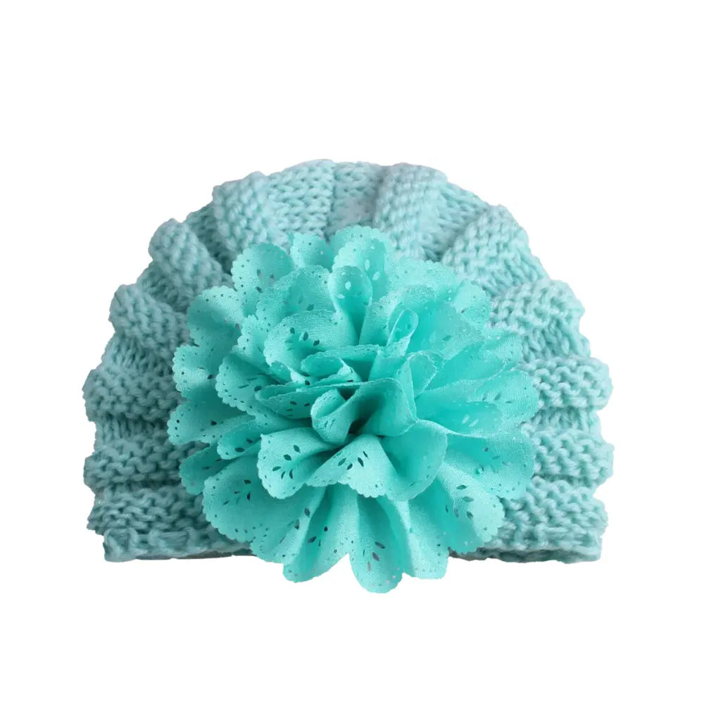 This versatile accessory from Alaya Junior, known as the Baby Girl Lace Flower Design Knitted Turban Cap (0m - 3 Yrs), features a light blue color and a large decorative fabric flower attached to the front for a charming touch.