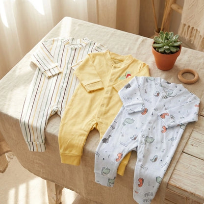 Three baby rompers on a table with a potted plant and wooden toy.