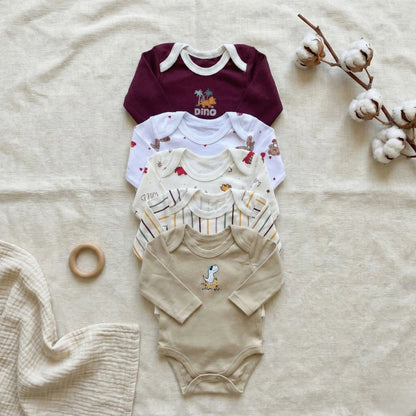 Collection of baby bodysuits on a textured surface with cotton branches.