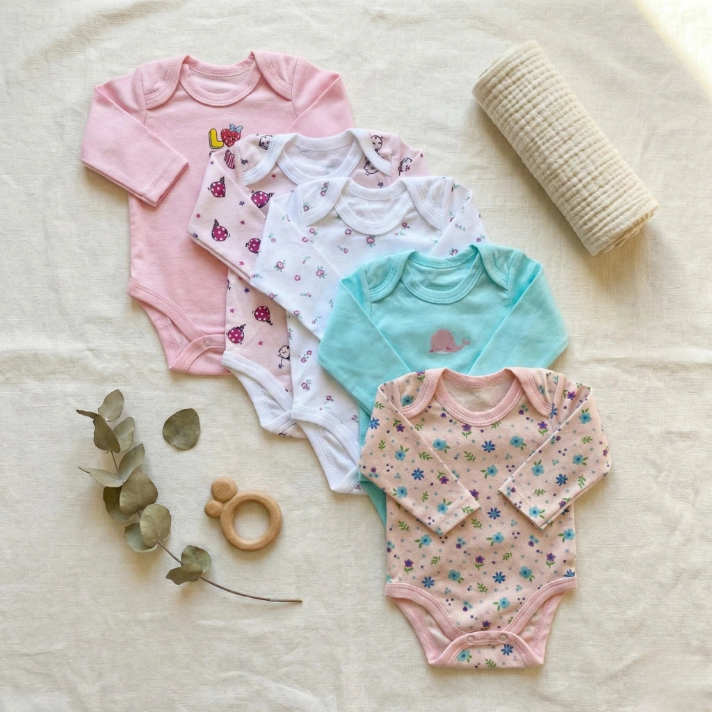Collection of colorful baby bodysuits on a soft surface with a teething ring and leaves.