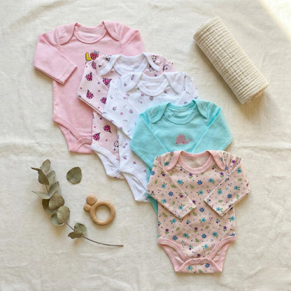 Collection of colorful baby bodysuits on a soft surface with a teething ring and leaves.