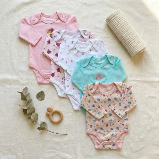 Collection of colorful baby bodysuits on a soft surface with a teething ring and leaves.