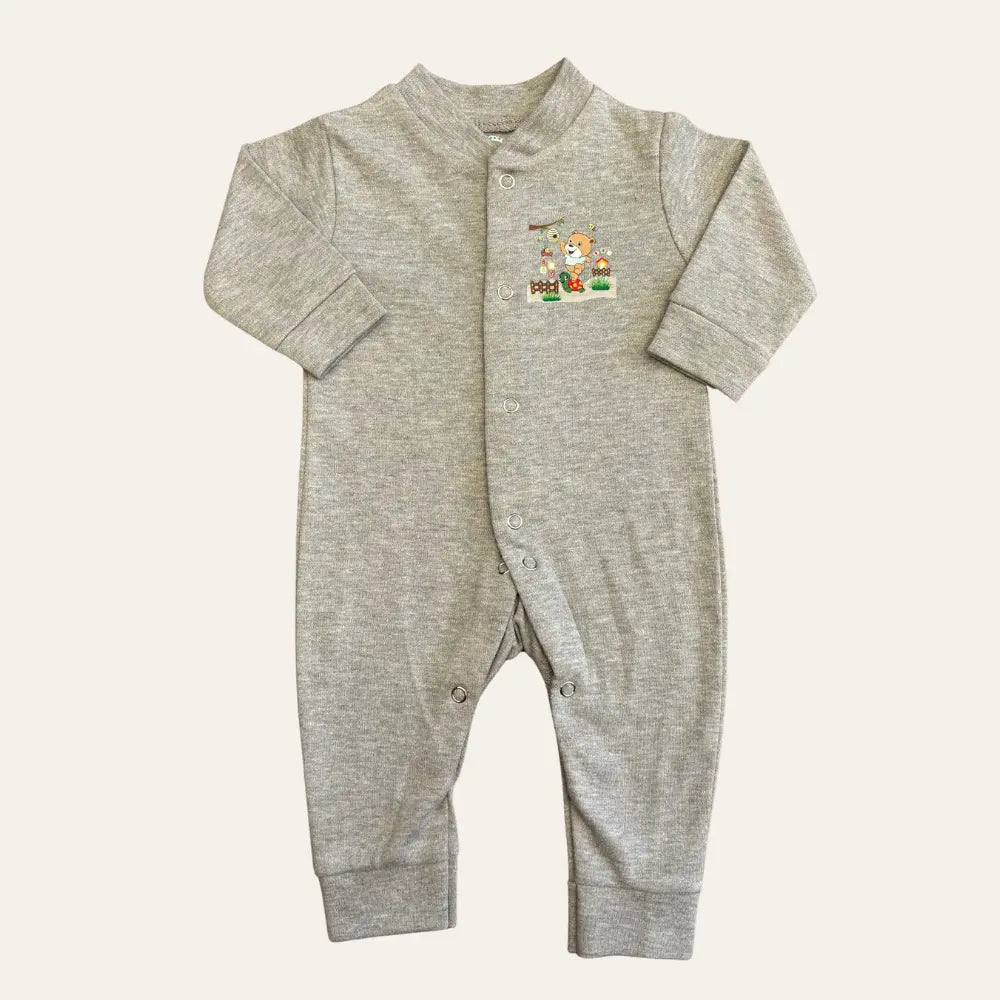 The Alaya Junior Carters Pack Of 3 Open Feet Romper in a peach and grey combination features a grey baby onesie with long sleeves and snap buttons down the front. It is adorned with a small, colorful embroidered patch on the chest that depicts two animals beside a tree and a small house. The soft and comfortable fabric makes it an ideal choice for newborn baby clothing in Pakistan.