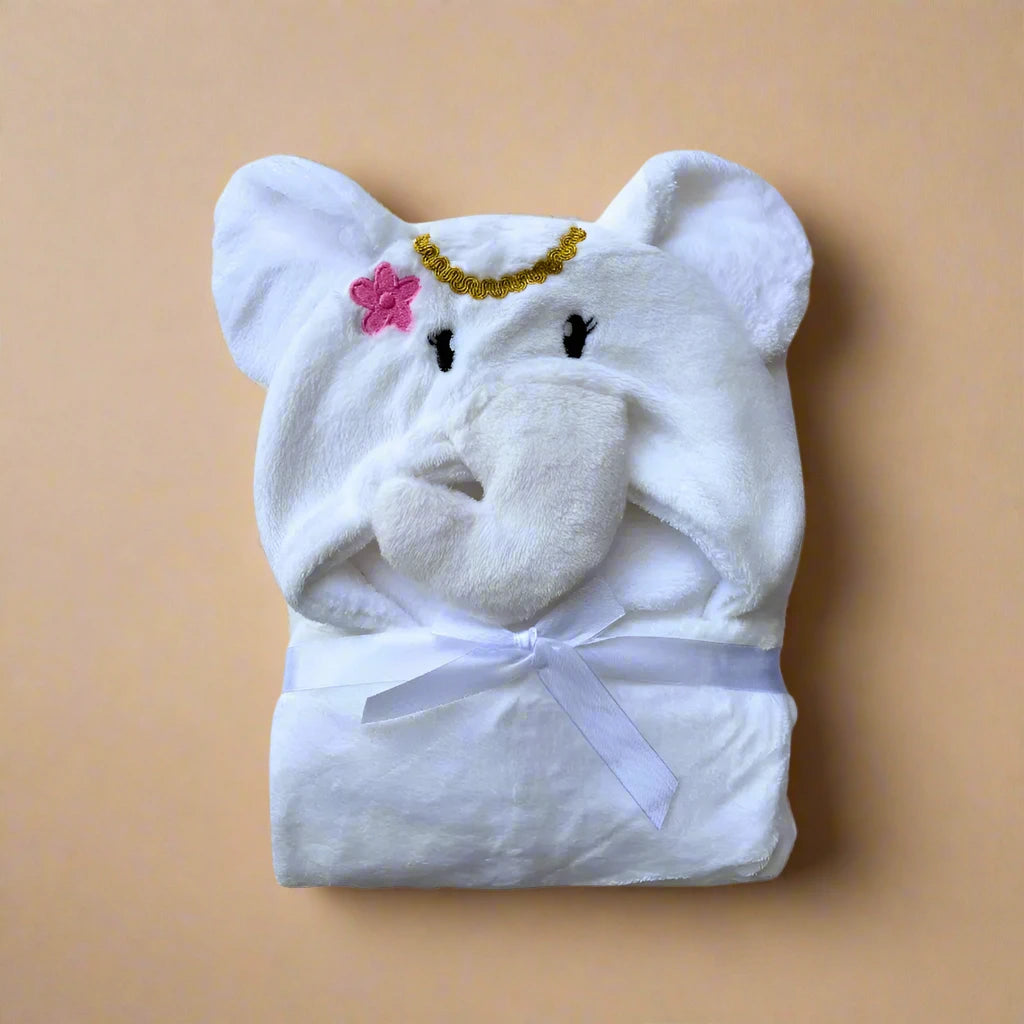 The Alaya Junior Character Hooded Blanket/Wrapping Sheet – Winter (100 x 70 cm) is a plush baby blanket folded neatly with a hood designed to look like an elephant's head, complete with ears, a trunk, and embroidered facial features. One ear has a pink flower, and there is a gold chain on the forehead. This versatile baby essential also features a white ribbon tie.