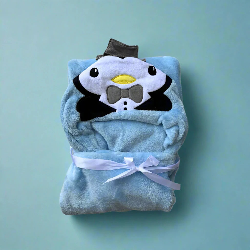 The Character Hooded Blanket/Wrapping Sheet – Winter by Alaya Junior, made of plush material, showcases a charming penguin face embroidered on the character hood design. The penguin is adorned with a gray bow tie and hat. The light blue blanket is neatly folded and secured with a white ribbon, set against a plain blue background.