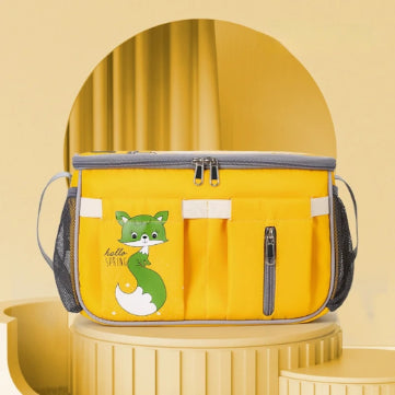 A yellow insulated lunch bag from Alaya Junior, featuring a cute green fox illustration with "hello spring" written near the fox. The bag is made from water-repellent material and has a grey zipper, side mesh pockets, front pockets. It is set against a matching yellow background with arches and rounded shapes.