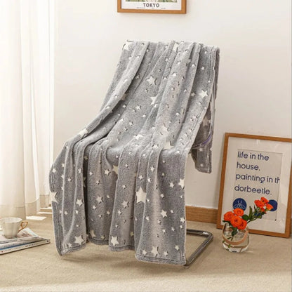 An inviting, ultra-soft Glow in the Dark Blanket by Alaya Junior, featuring butterfly and star patterns, is elegantly draped over a sleek modern metal chair in a well-lit room. The space also showcases a framed inspirational quote resting on the floor, a small vase with vibrant orange flowers, and a cup on a saucer carefully placed on the beige carpet.