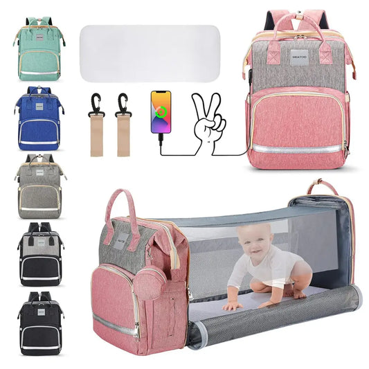 Introducing the Alaya Junior's HEATOO Baby Diaper Bag with Changing Station, a 3-in-1 large capacity travel bag available in pink. The bag showcases a built-in bassinet, as seen with a smiling baby comfortably lying inside. Additional color options include green, blue, black, and grey. This versatile portable changing station comes equipped with a USB port, stroller hooks, and plenty of pockets for optimal organization.