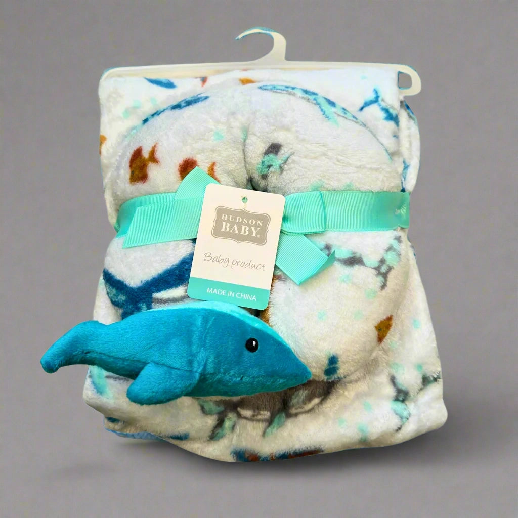 Baby blanket with whale toy and Hudson Baby tag on a white background