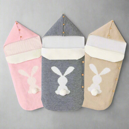 Three baby swaddle blankets with bunny designs in pink, gray, and beige on a white background.