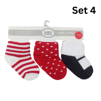 A set of three baby socks labeled "0-12 months" from "Hudson," featuring a stay-on design and soft, stretchy fabric. The socks hang on a cardboard strip; one is red and white striped, another is red with white polka dots, and the third is black and white. Text in the image reads "Luvable Baby 3-Pair Socks Gift Set.