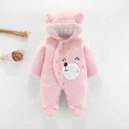 The Snuggly Bear Hug: Plush Hooded Romper for Babies by Alaya Junior is a pink romper designed to resemble a teddy bear. It features a hood with ears, an embroidered bear face on the front, and covered feet. This winter baby clothing item is made of plush fabric and displayed on a white background alongside a small bundle of wheat.