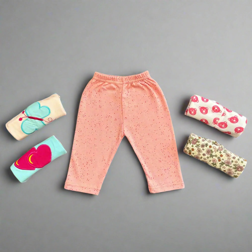 A pair of pink Alaya Junior baby girl trousers with elastic waistbands and small colorful dots is displayed on a gray surface, surrounded by four rolled-up pairs from the Pack of 5 Baby Girl Trousers in various colors and adorable designs, including patterns with butterflies, hearts, mushrooms, and floral prints.