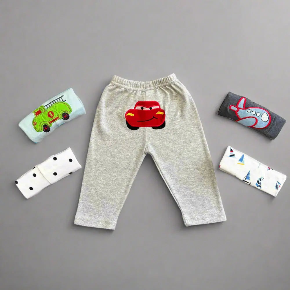 Introducing the Pack of 5 Unisex Baby Trousers with Colorful Vehicle Embroidery from Alaya Junior. These soft and comfortable trousers feature playful designs, including a red car on a gray background, a green vehicle, a red airplane, black dots, and charming sailboats. Perfect for adding charm to any little one's wardrobe!