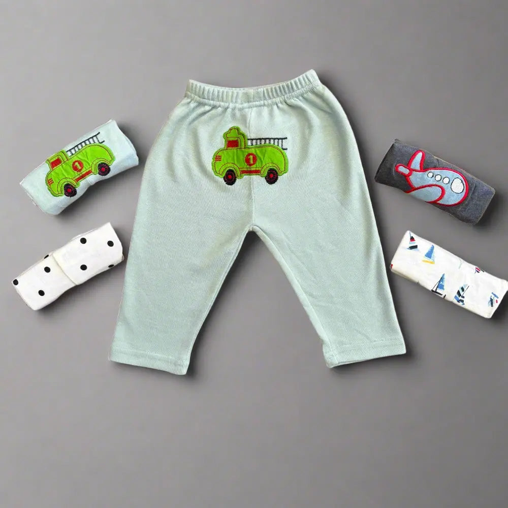 The light green toddler pants from Alaya Junior's Pack of 5 Unisex Baby Trousers feature a soft and comfortable fire truck design prominently displayed against a gray background. These unisex baby trousers are complemented by four pairs of rolled-up socks in assorted colors and patterns, including polka dots, an airplane, and abstract designs.